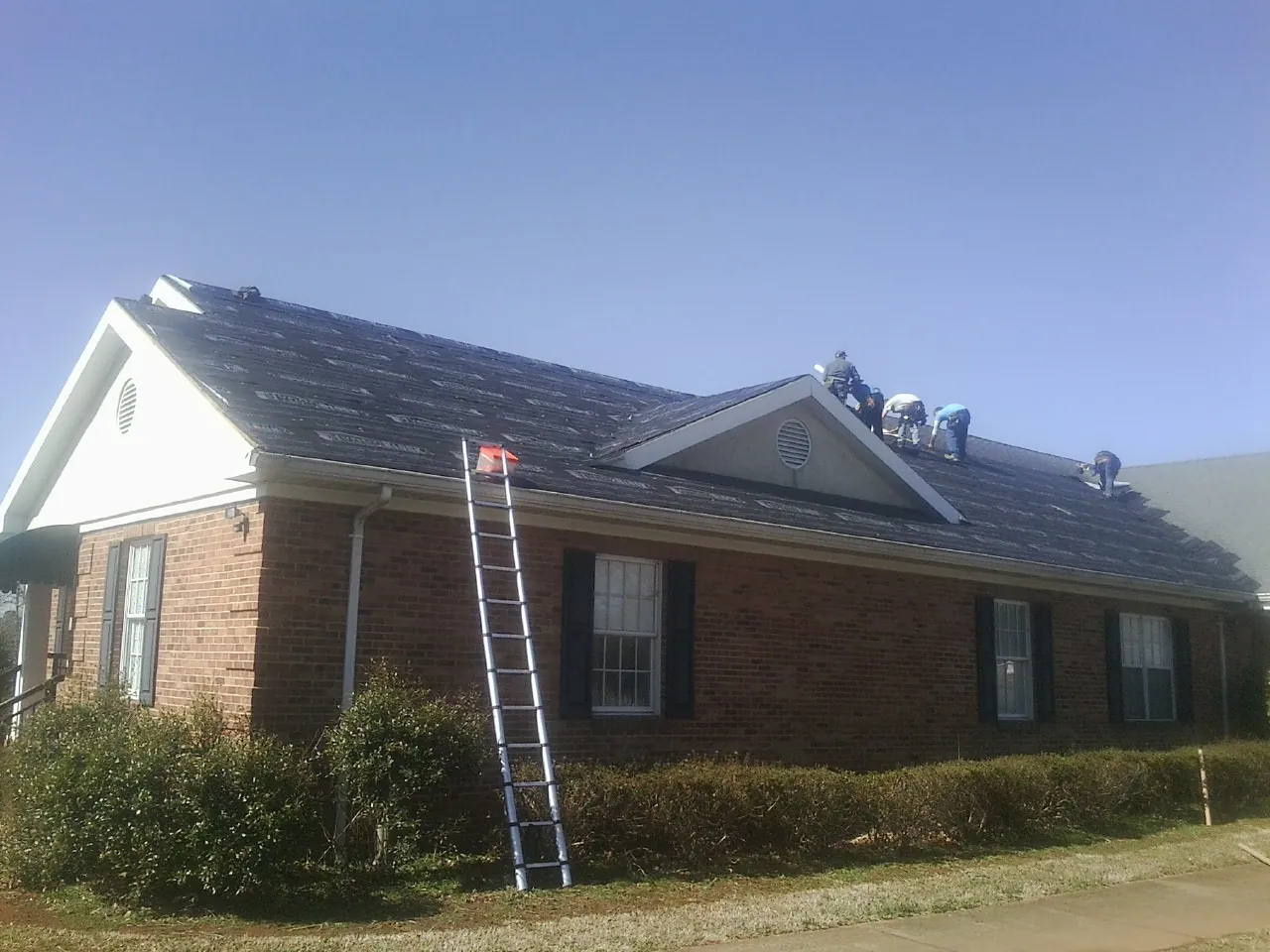 Crew tearing shingles off a brick ranch roof with a ladder set — Emergency Roof Repair work by our crew in East Saint Louis