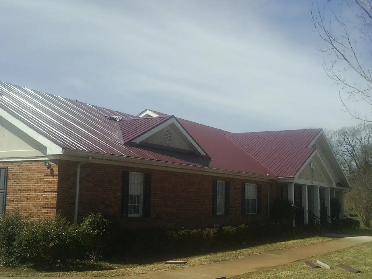 Red metal roof with gabled entries on a long brick building, from a Hail Damage Roof Repair job in East Saint Louis