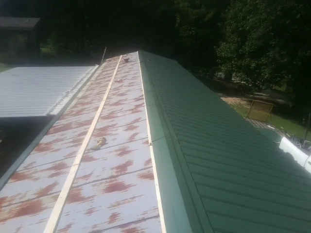 Old rusted panels beside newly installed green metal roofing — Wind Damage Roof Repair by Roofing Brothers in East Saint Louis