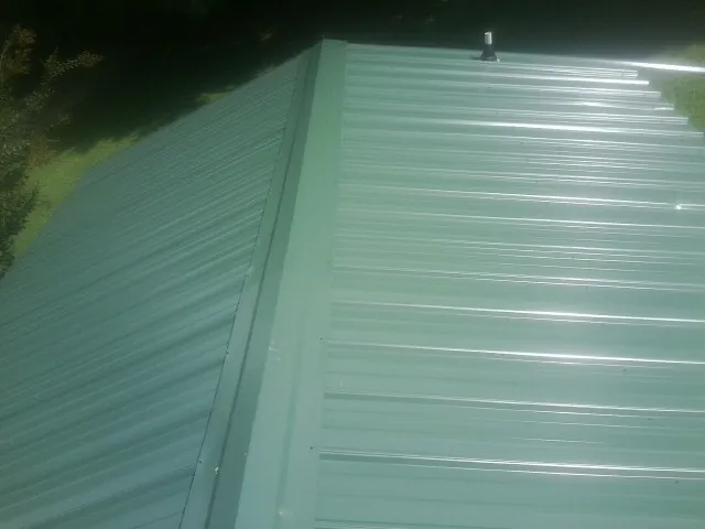 New green metal panels meeting at the ridge of a roof — Flat Roof Repair work by our crew in East Saint Louis