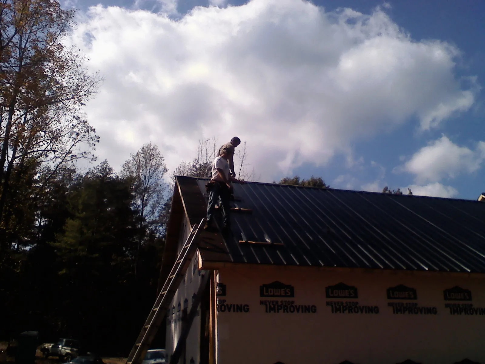 Roofer fastening dark metal panels high against a cloudy sky, from a Roof Inspection job in East Saint Louis