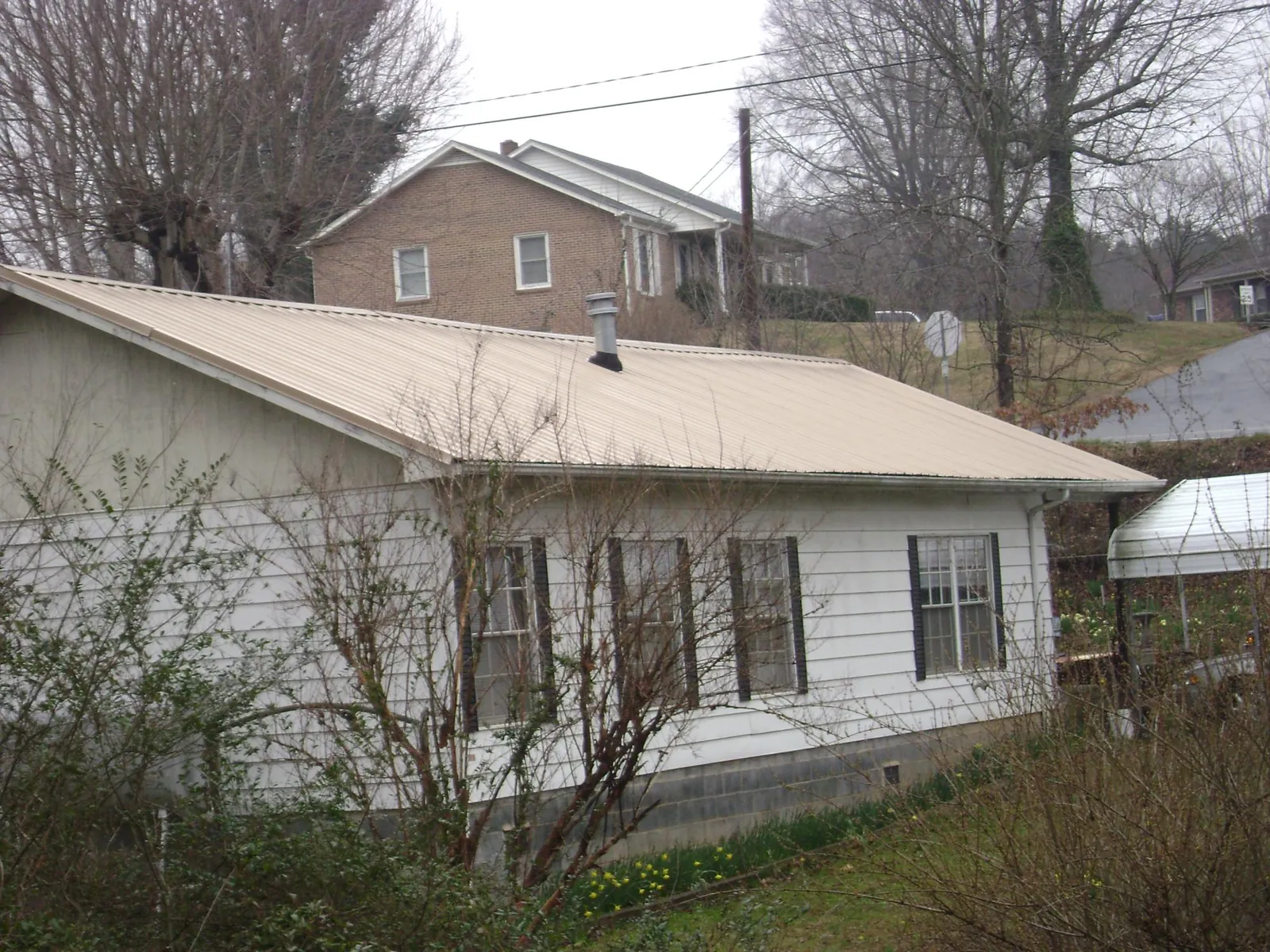 Tan metal roof on a white sided house set into a hillside — Commercial Roofing by Roofing Brothers in East Saint Louis